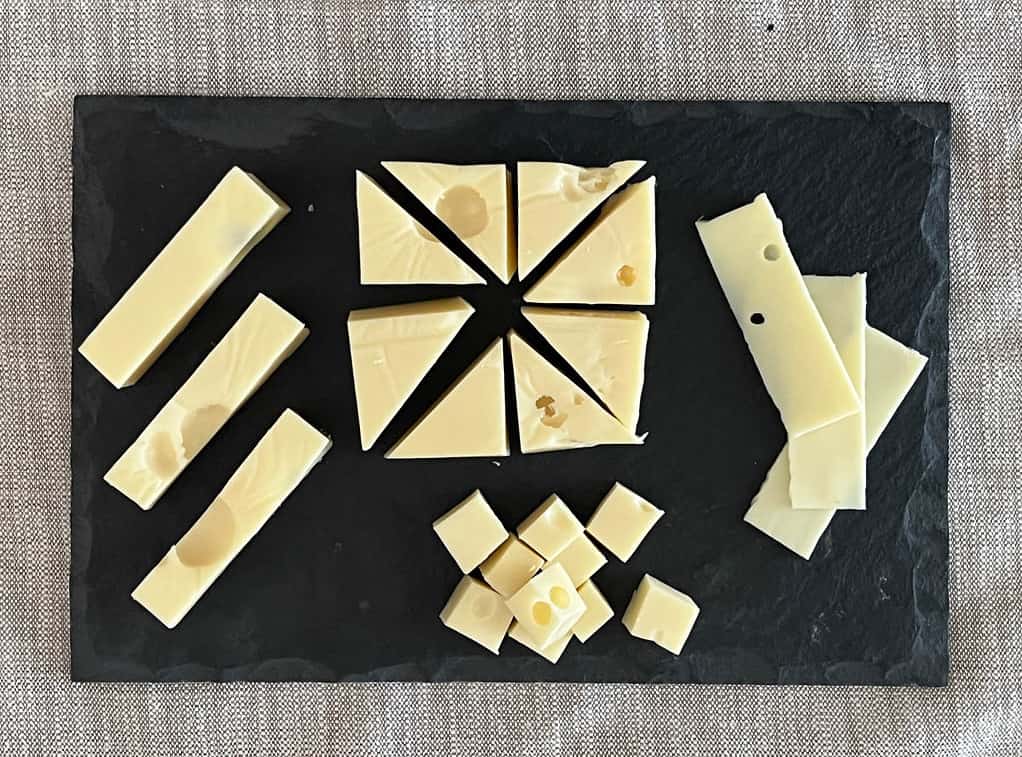 Cheese plate with swiss cheese cut into thin slices, cubes, wide sticks and triangles on a slate