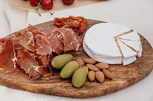 brie cheese with nuts, olives and meats on a wood board