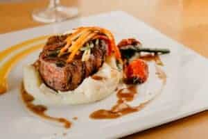 Beef steak atop a mound of mashed potatoes, topped with matchstick carrots and a silky brown gravy.