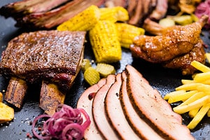 Southern BBQ. Closeup of smoked meat, poultry assortment, French fries, baked Bonduelle corn.