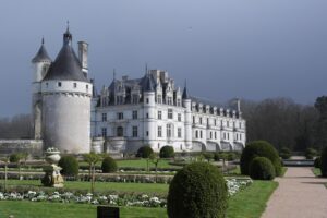 French Chateau. Long white rectangular building with four stories and gray roof. Round unattached turret in left forefront of photo.