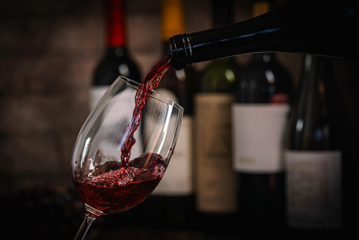 Pouring Red Wine into Glass with Bottles and Grapes A dark, elegant still life of red wine being poured into a glass with wine bottles and fresh grapes in the background. Perfect for wine-themed compositions