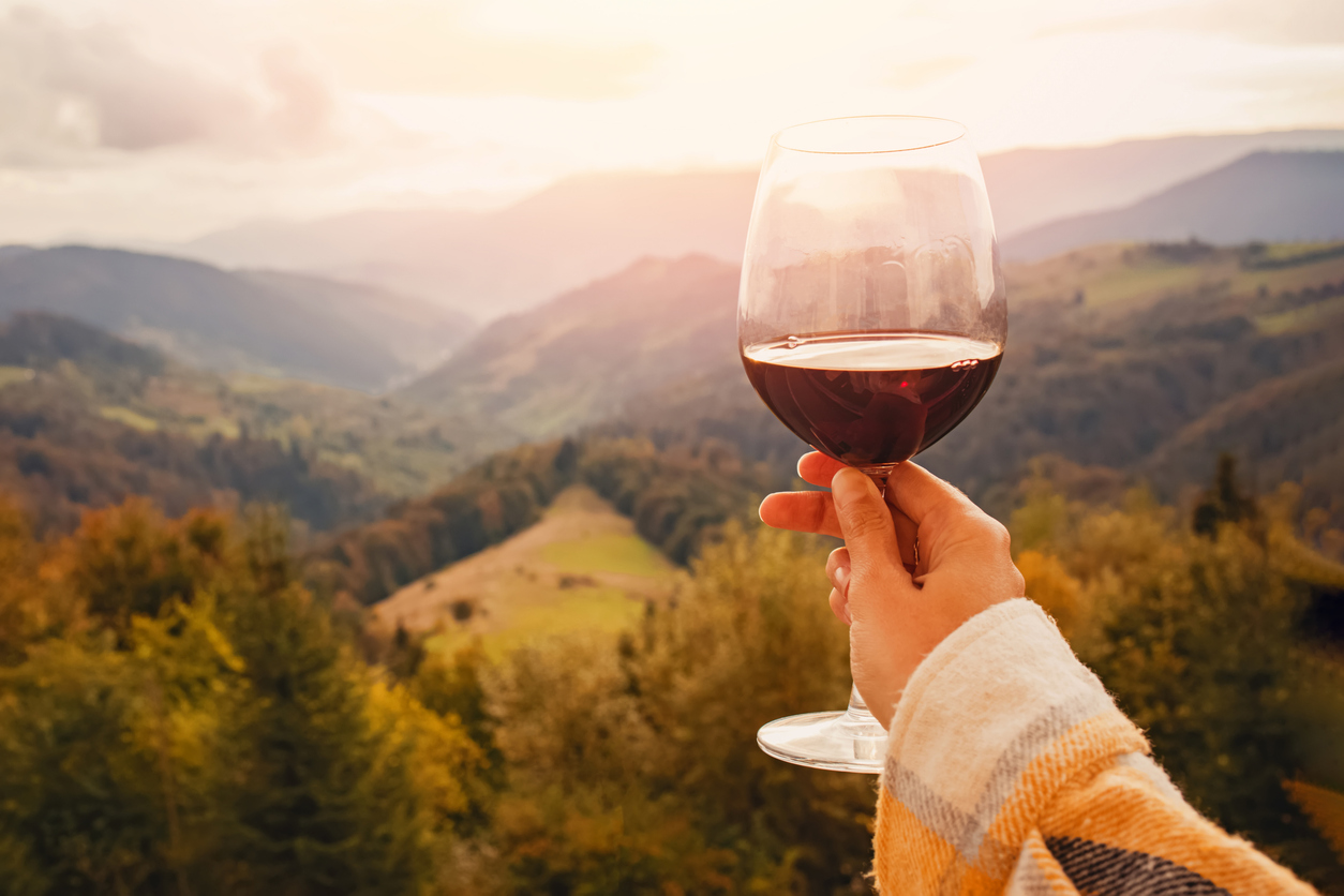 Woman’s hand holding a glass of red wine with a mountain view. Woman's hand holding a glass of red wine with a beautiful view to autumn mountains