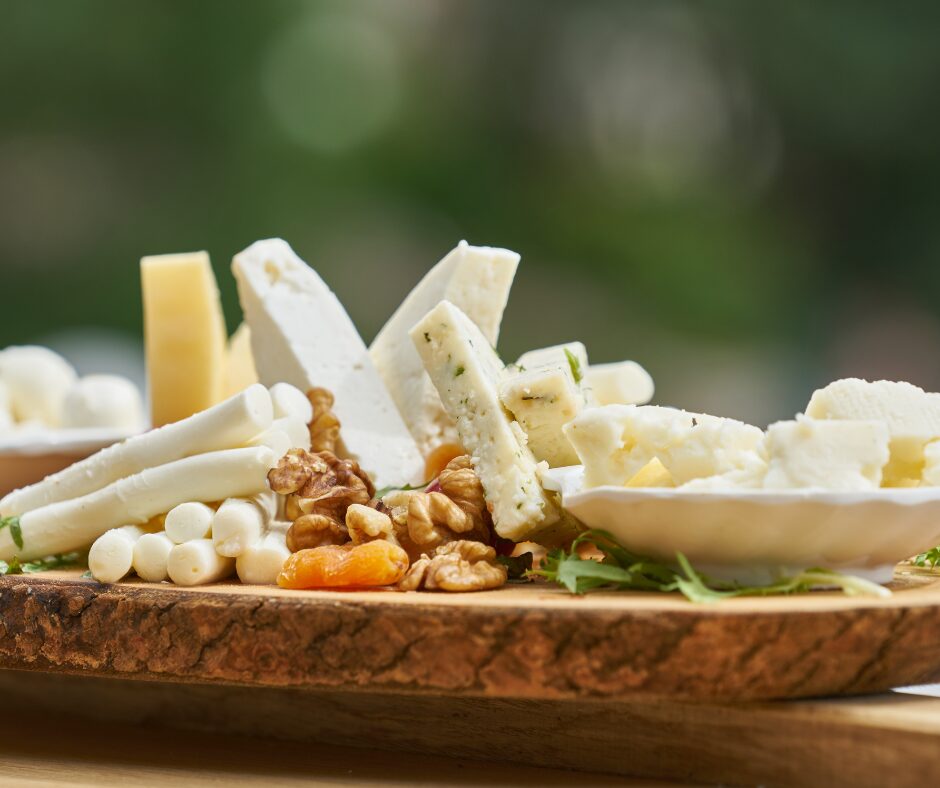 Wood board or white cheeses. Some are in cylinders, slices and wedges, displayed with dried apricots and nuts.