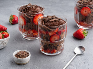 clear glasses filled with dark chocolate mousse and sliced strawberries on a gray table