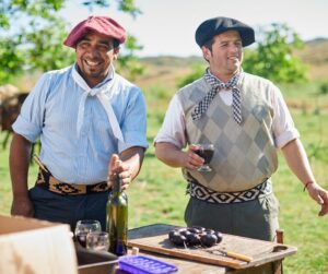 Two gauchos from Argentina standing holding glasses of dark red wine. Each wears a beret-like hat