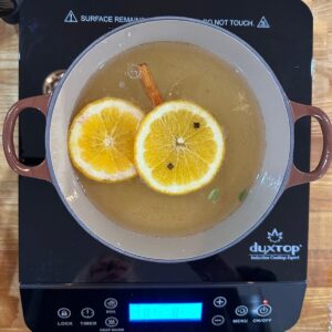 Mulled White wine in a brown pot simmering with lemon and orange slices, cloves and cinnomon sticks
