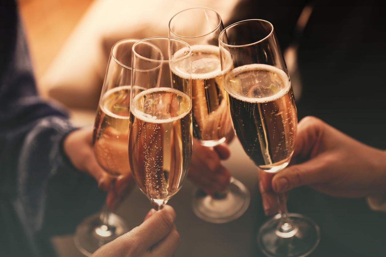 People clinking glasses with sparkling wine indoors , closeup Four flutes of sparkling wine clinking together for a toast