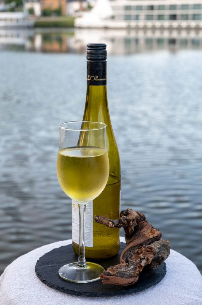 Tasting of white quality riesling wine served on outdoor terrace in Mosel wine region with Mosel river and old German town on background in sunny day, Germany
