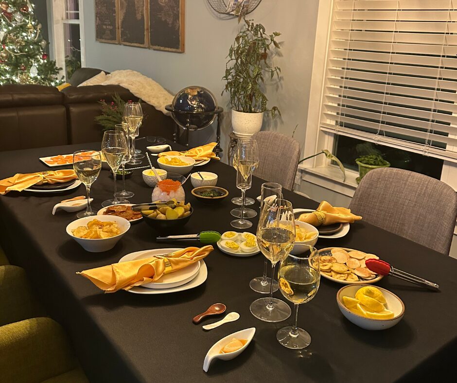 Vertical View of Table with Bubbly and Flat Full shot of table set with black table cloth, gold linens and dishes with blinis, develed eggs, salmon roe over ice, creme fraiche, herbs and more