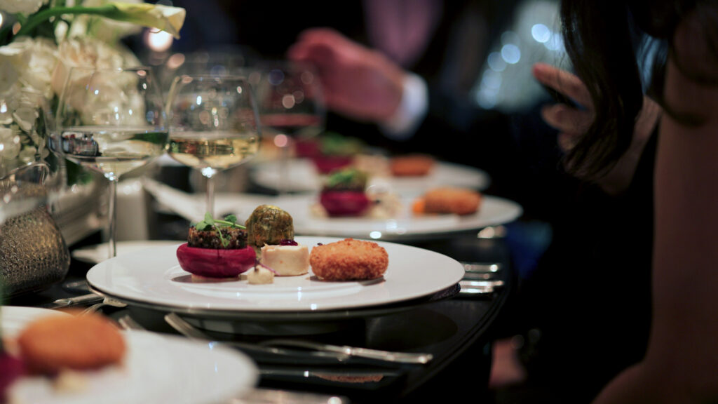 A beautifully plated gourmet dish served at a sophisticated event, accompanied by fine wine and elegant table settings. The dim lighting and luxurious ambiance create an intimate dining atmosphere. Perfect for themes related to fine dining, luxury events, and gastronomy. Guests indulging in fine wine and exquisite cuisine at an elegantly decorated restaurant. A beautifully plated dinner set on a luxurious table, creating the perfect ambiance for a memorable wedding celebration.