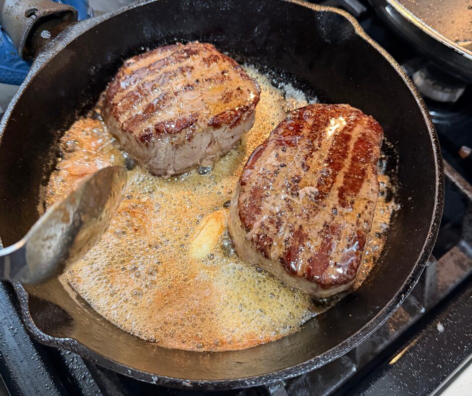 Two pieces of beef tenderloin being basted in butter in a cast iron skillet