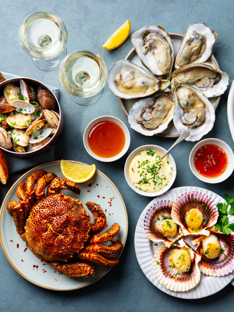 Seafood buffet, crab, oysters, scallops with white wine on blue background. Top view.