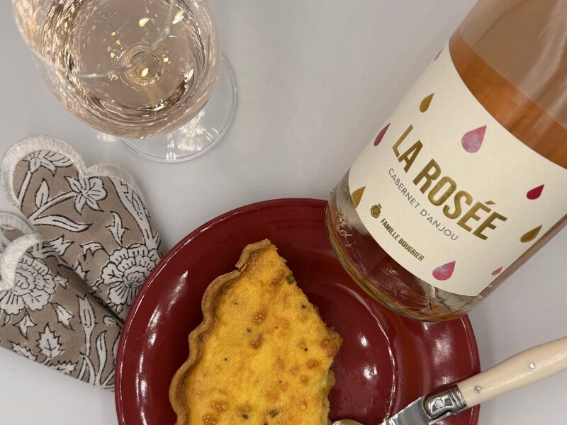 Bottle of Rosé d'Anjou next to a plate of a slice of ham and cheese quiche and a glass of the Rosé