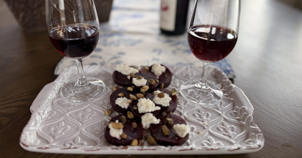 Two glasses of Cabernet Franc on a white fleur-des-lis platter with two rows of Beet and Goat Cheese Salad with Pistachio nuts and a drizzle of olive oil