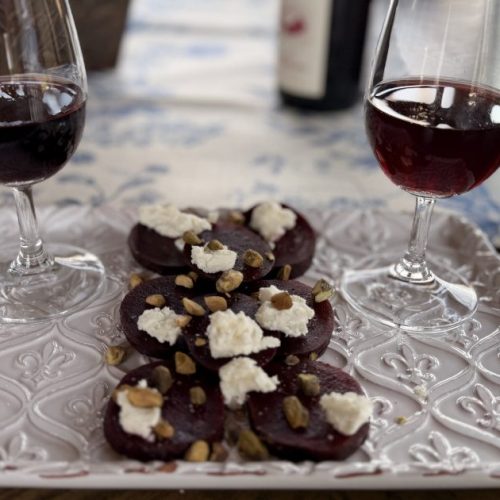 Two glasses of Cabernet Franc on a white fleur-des-lis platter with two rows of Beet and Goat Cheese Salad with Pistachio nuts and a drizzle of olive oil