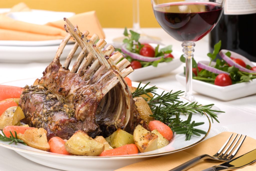 Rack of Lamb (ribs) with Rosemary garlic dressing, garnished with baby carrots, potatoes and rosemary sprigs. Dinner settings.