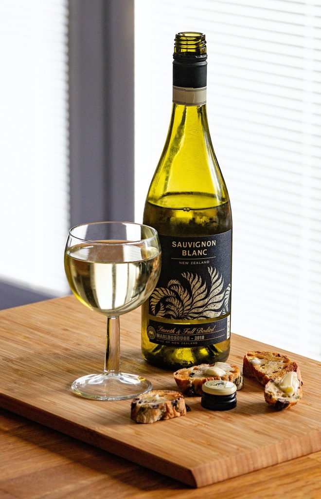 Marlborough Sauvignon Blanc wine bottle and glass almost filled in front of a sunny window, sitting on a wood board