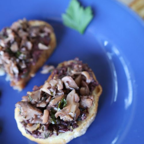 Royal blue plate with two crostinis of mushroom and olive tapenade with a sprig of parsley on the plate