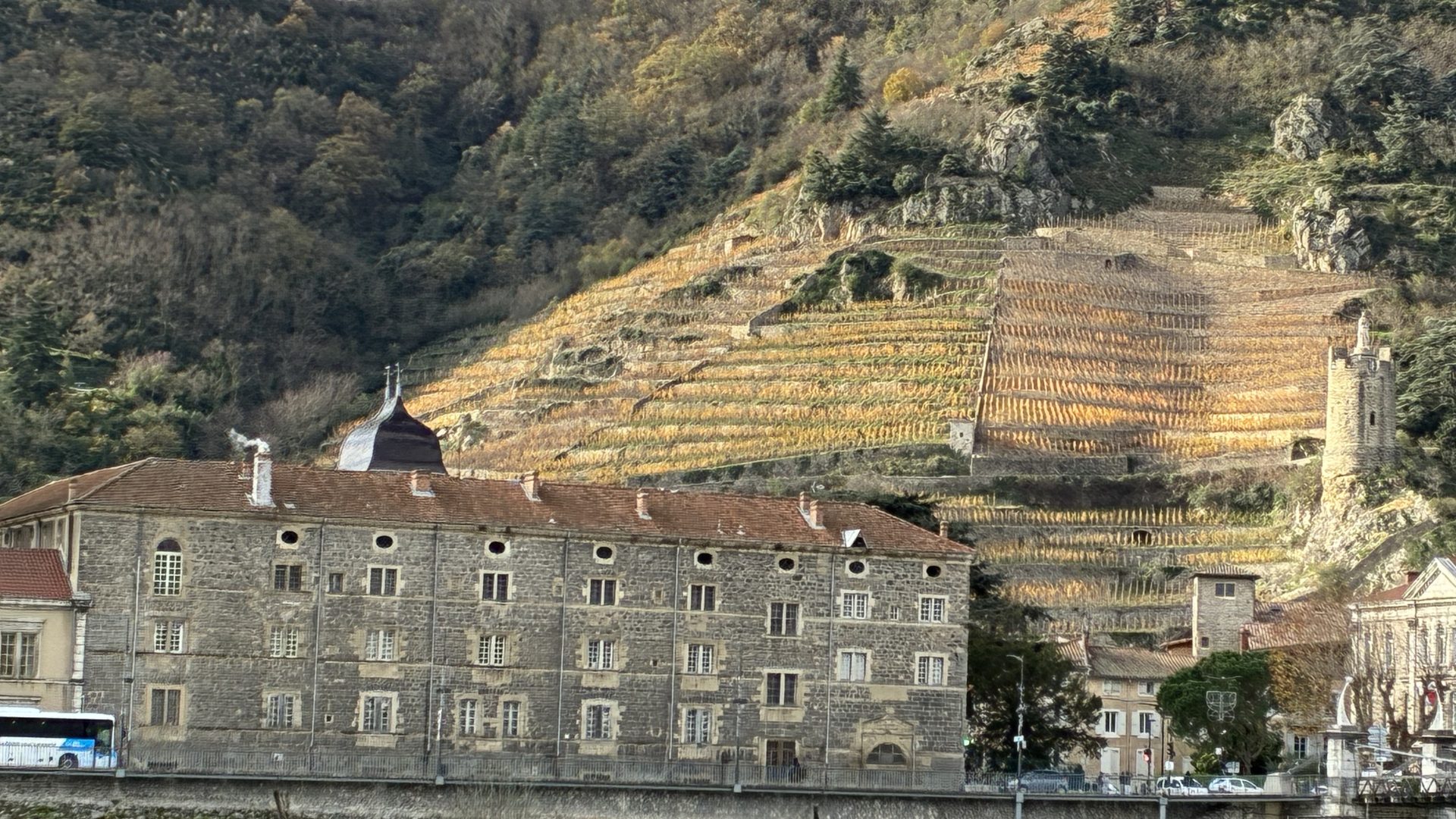 Northern Rhone Terraced Vineyards 1920×1080 Image of a four story building on the Rhone River with terraced vineyard steeply angling up behind