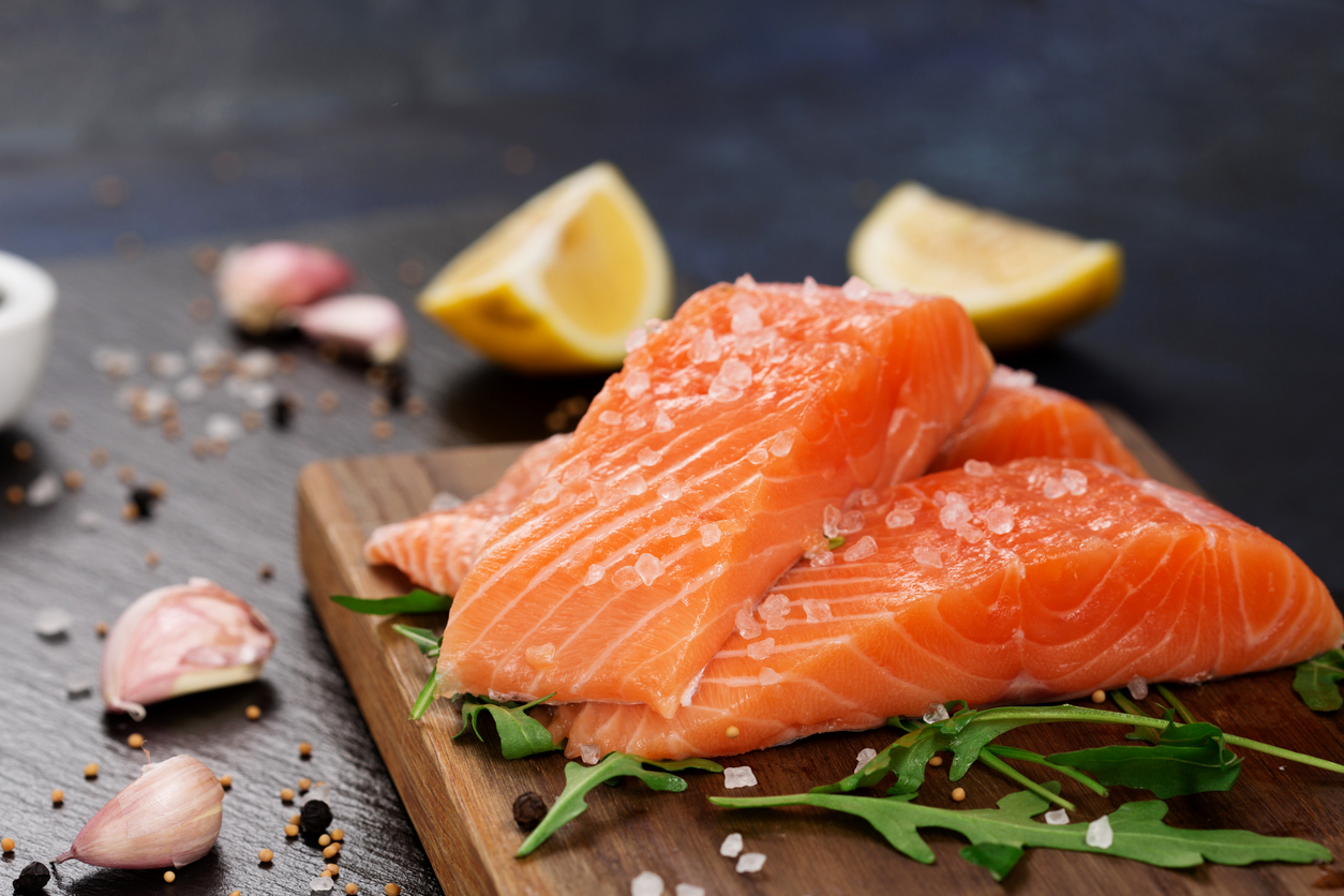 Raw fillet of salmon with sea salt, lemon and pepper on black stone background. Raw fillet of salmon with sea salt, lemon and pepper on black stone background. Fresh fish prepared for cooking. Top view, copy space. Healthy Brain Food concept.