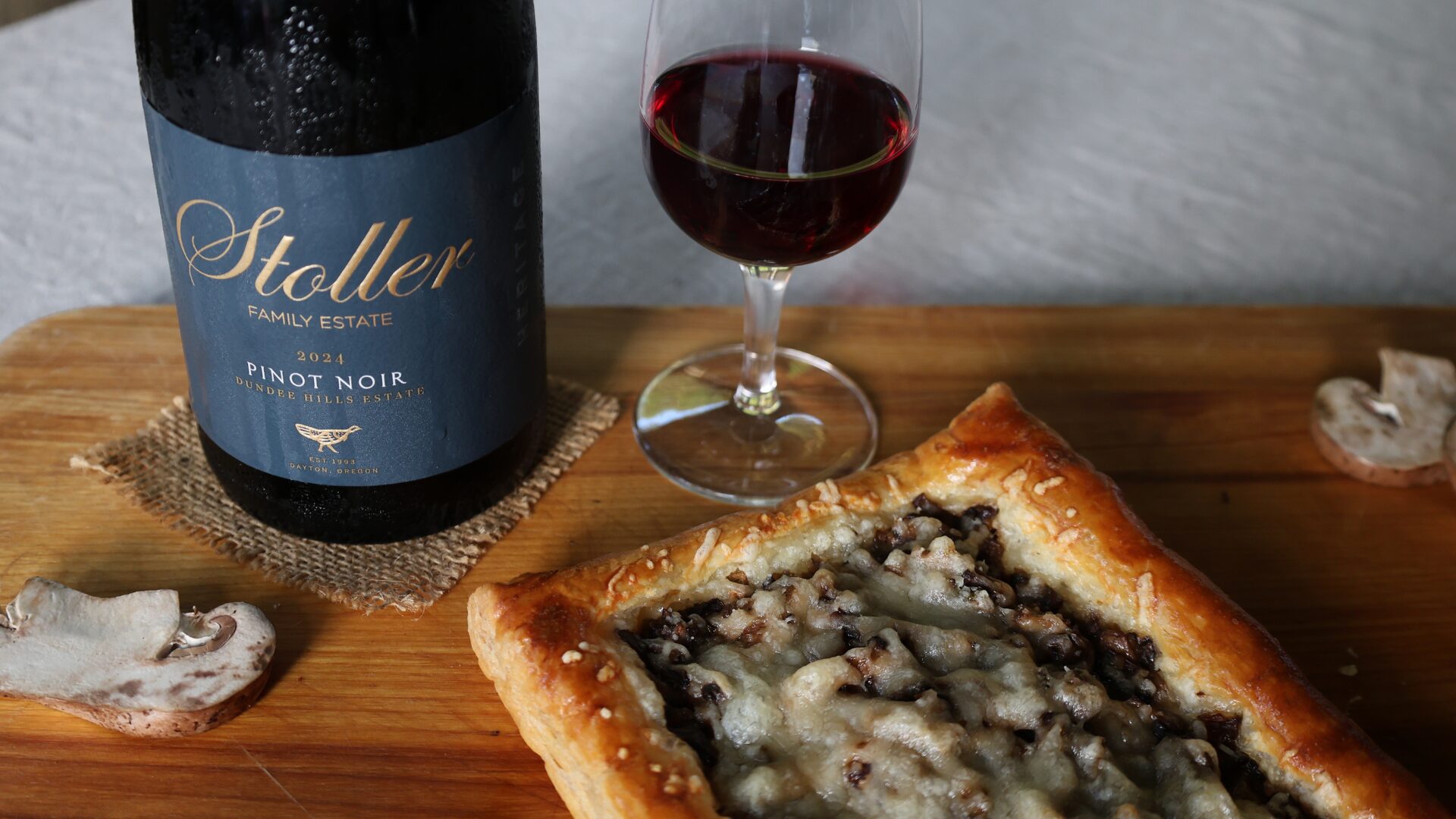 Chilled Pinot Noir with Tart 1920×1080 Chilled bottle of Pinot Noir on a wood board next to a light ruby glass and a Mushroom Gruyere Tart - on a hot July evening. Condensation is running down the front of the wine bottle. Raw mushrooms are skewn around the board.